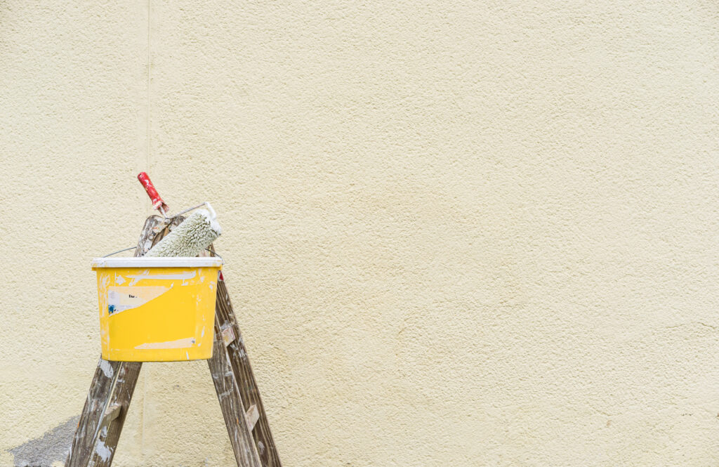 Painter ladder with bucket and paint roller in front of an exterior wall painting safety - ladder